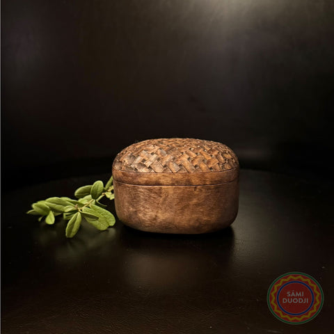 Ask i björk av Duodji-sameslöjdare Sven-Åke Risfjell Vilhelmina.&nbsp; Den har det samiska färdskrinet Kisans form. Längd 8,8 cm, bredd 8,5 cm och höjd 6 cm. Det välvda locket är dekorerad med ett flätmönster i karvsnittsgravyr. Askens form är inspirerad av det samiska färdskrinet Kisan.