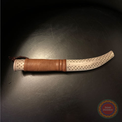En sydsamisk halvhornskniv i form och sydsamisk gravyr av Same/Duodjislöjdare Sven-Åke Risfjell från Vilhelmina i Södra Lappland. Knivens hela längd är 24.5 cm. Knivskaftet och hölstret är i renhorn  Bladet är smitt av Sven-Åke i kolstål med längd 95 mm. Knivens upphängningsanordning är gjord  i tvinnat renskinn.  Risfjells Sameslöjd i Vilhelmina Södra Lappland