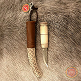 En sydsamisk halvhornskniv i mindre modell med sydsamisk gravyr av Same/Duodjislöjdare Sven-Åke Risfjell från Vilhelmina i Södra Lappland. Knivens hela längd i hölstret är 20 cm. Knivskaftet och hölstret är i renhorn. Det smidda bladets längd är 62 mm. Knivens upphängningsanordning är i tvinnat renskinn. Risfjells Sameslöjd i Vilhelmina södra Lappland.