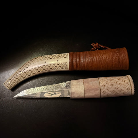 Halvhornskniv med sydsamisk form och gravyr i design av Same/Duodjislöjdare Sven-Åke Risfjell från Vilhelmina i Södra Lappland. Knivens hela längd är 26 cm. Knivskaftet är i renhorn och även det med sydsamisk gravyr. Bladet i damasksmide är tillverkat av Mikael Styrefors. Bladets längd är 10 cm. Knivens upphängningsanordning är gjord i tvinnat renskinn. Risfjells Sameslöjd Vilhelmina