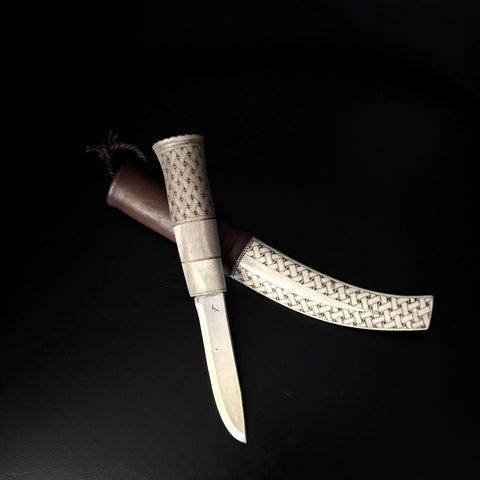 Halvhornskniv med sydsamisk form och gravyr i design av Same/Duodjislöjdare Sven-Åke Risfjell från Vilhelmina i Södra Lappland. Knivens hela längd är 25 cm. Knivskaftet är i renhorn och även det med sydsamisk gravyr. Bladet i kolstål tillverkad av Sven-Åke. Bladets längd är 9,5 cm. Knivens upphängningsanordning är gjord i tvinnat renskinn.