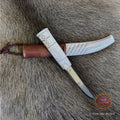 En sydsamisk halvhornskniv med sydsamisk gravyr av ©Same/Duodjislöjdare Sven-Åke Risfjells egen mönsterkomposition. Knivens hela längd i hölstret är 24 cm. Knivskaftet och hölstret är i renhorn. Det smidda bladets längd är 98 mm. Knivens upphängningsanordning är i tvinnat renskinn. Risfjells Sameslöjd i Vilhelmina södra Lappland.