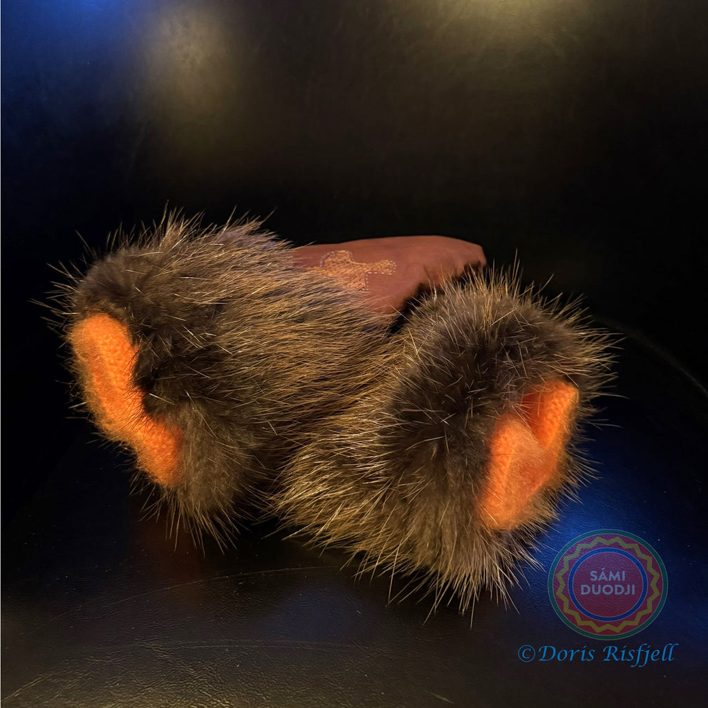 Renskinnshandskar med bräm av bäverskinn av sameslöjdare Doris Risfjell, Risfjells Sameslöjd Vilhelmina. Handskarna har en dekoration av en ripa i laxskinn. Innervanten som är stickad i mohair gör handskarna extra varma, mjuka och sköna. Här i orange garn. Storlek 7-8 liten dam. Risfjells Sameslöjd i Vilhelmina.