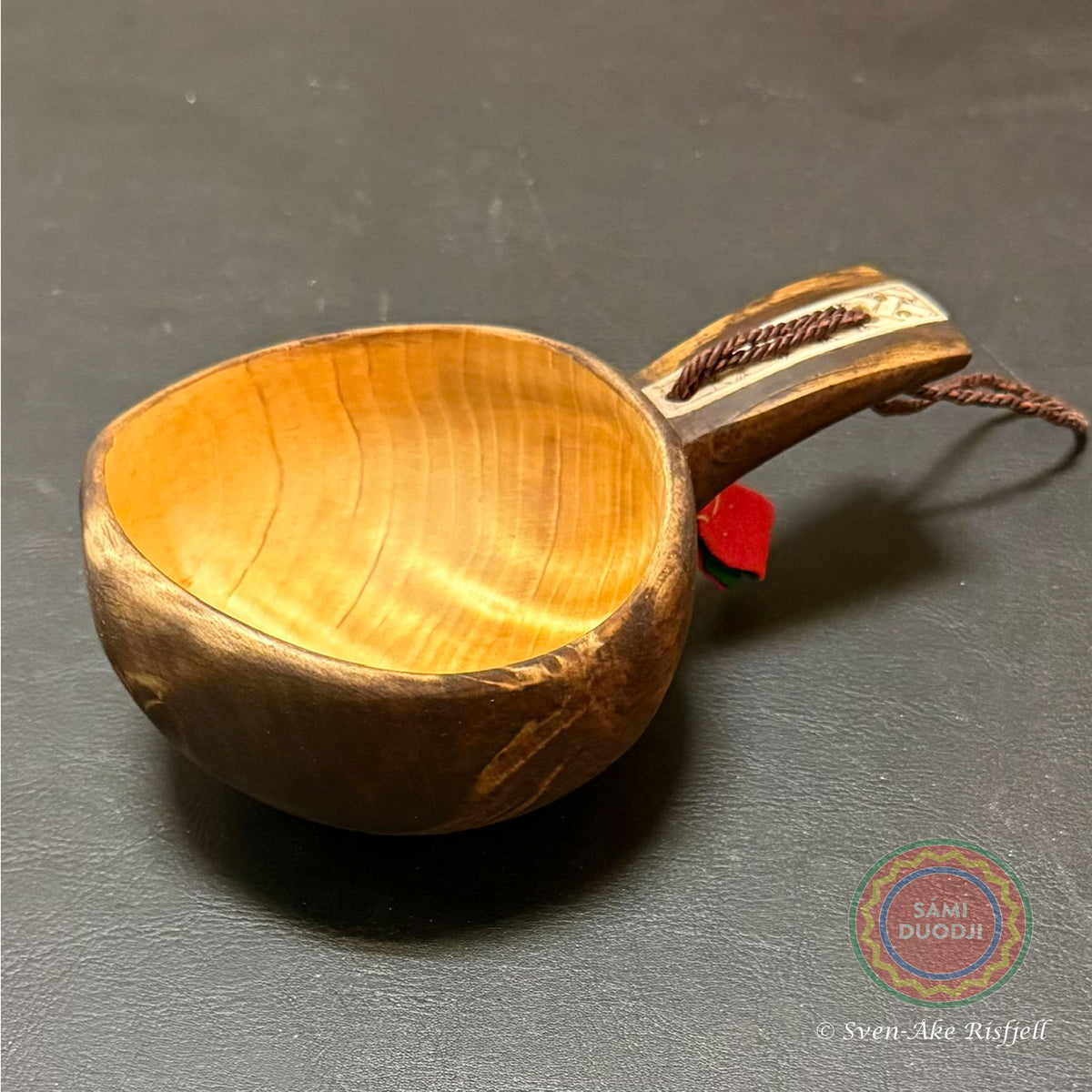 Kåsa ur björkvril med horninlägg och sydsamisk mönstergravyr av Duodji sameslöjdare Sven-Åke Risfjell Vilhelmina. Kåsans längd är 15,5 cm och diameter 9,5 cm. Höjden på kåsan är 4,5 cm. Den rymmer 1,5-2 dl, Risfjells ameslöjd i Vilhelmina, södra Lappland.