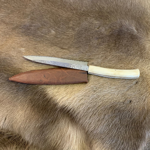 Kockkniv med renhornsskaft och sparsmakad gravyr av same-Duodjislöjdare Sven-Åke Risfjell, Vilhelmina. Knivens längd är 34,5cm lång inne i hölstret. Knivbladet är japanskt smide 18,5 cm. Tunt blad.
