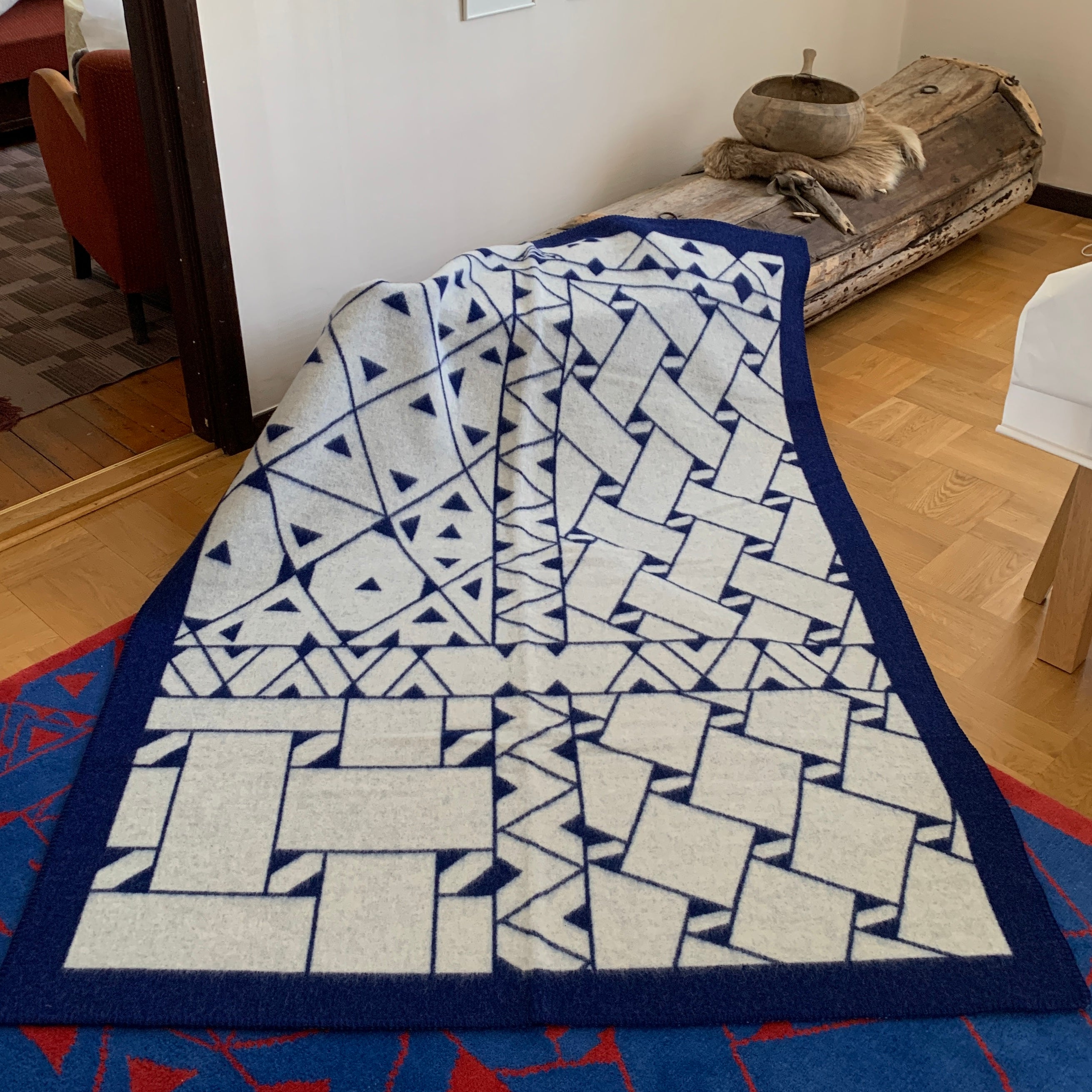 Pläd i ull. En unikt designad pläd av sameslöjdarna Doris och Sven-Åke Risfjell Vilhelmina Risfjells sameslöjd. Det gamla Nåjdmönstret från Marsfjäll återbördat i slöjden igen av Sven-Åke Risfjell och i textil produktion av Doris Risfjell. Här i blåvit-vit färgställning.