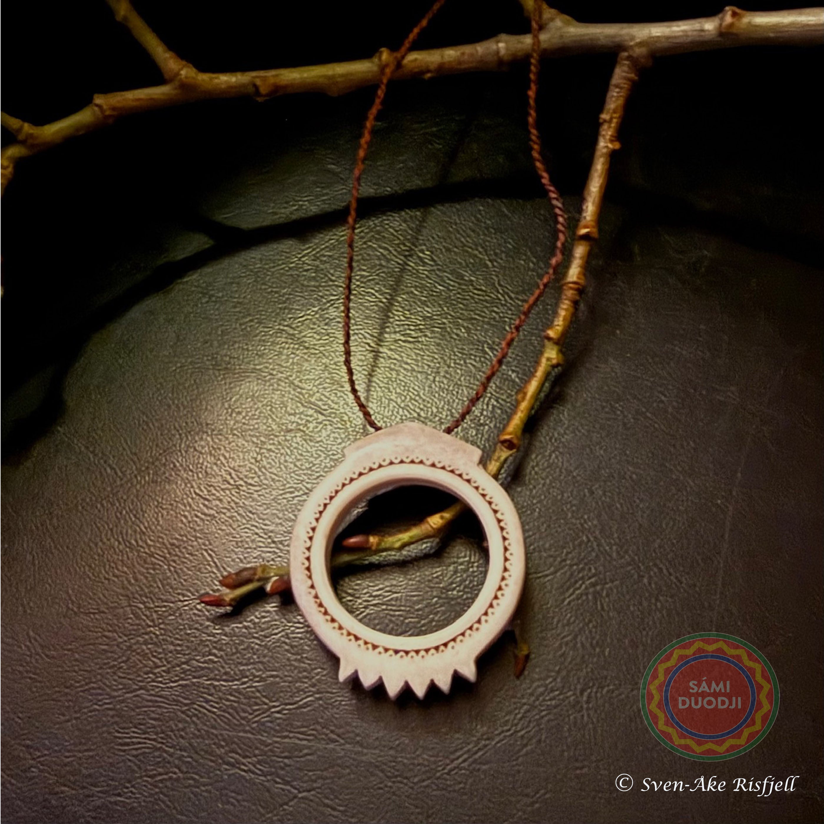 Malja Solens hustru unikt i horn, i Sven-Åke Risfjells egen design. Maljan är ett av de äldsta samiska kultursmyckena som vanligtvis är gjorda i silver men här har Sven-Åke Risfjell valt att göra dem i horn. Halsrem i tvinnat renskinn med en hornknapp. Ringens diameter är 48 mm. Mittpartiets längd 55 mm. Risfjells Sameslöjd i Vilhelmina, södra Lappland