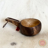 En kåsa ur björkvril med horninlägg i skaftet av same/Duodjislöjdare Sven-Åke Risfjell. Gravyren är av sydsamisk tradition. Kåsan rymmer 1,5-2 dl. Koppens diameter 9 cm. Kåsans längd är 15,5 cm och höjd 5 cm. Tvinnad rem av renskinn med tofs i kläde i rött och grönt. Risfjells Sameslöjd i Vilhelmina, södra Lappland