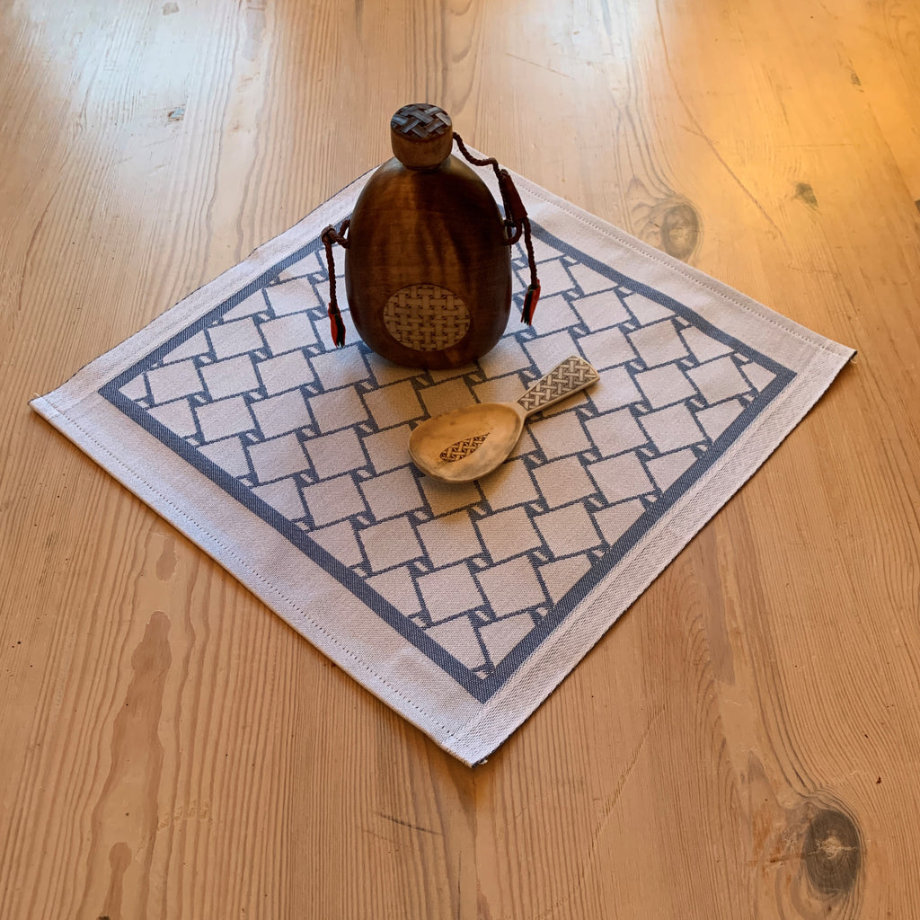 En bordstablett eller servett med nr tre av de tre sydsamiska flätmönster som går att återfinna på Marsfjällsnåjdens Daaskoe-väska som Sven-Åke Risfjell har satt ljus på i sin detaljstudie av väskan som han hittade tecknad i en bok i slutet av 1990-talet.  Här blå fläta på vit botten.