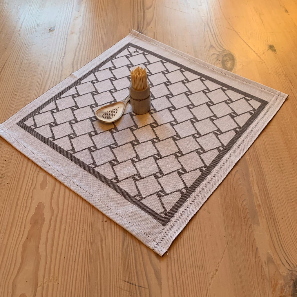 En bordstablett eller servett med nr tre av de tre sydsamiska flätmönster som går att återfinna på Marsfjällsnåjdens Daaskoe-väska som Sven-Åke Risfjell har satt ljus på i sin detaljstudie av väskan som han hittade tecknad i en bok i slutet av 1990-talet.  Här grå fläta på vit botten.