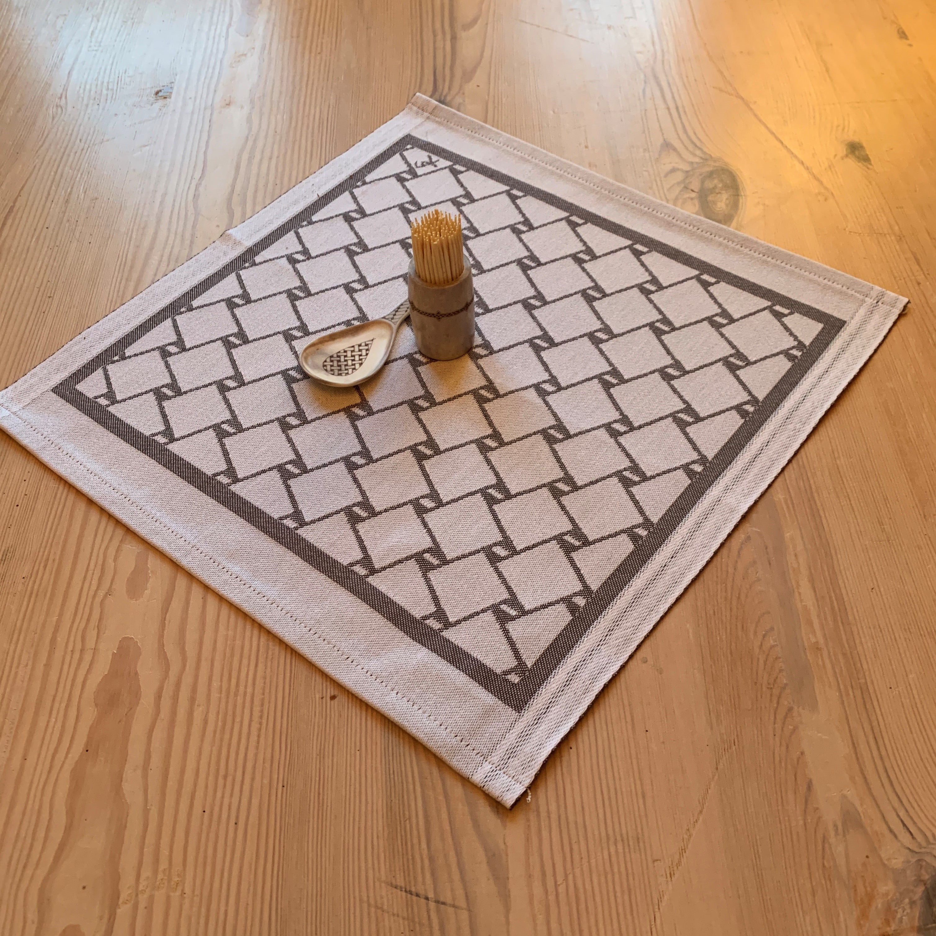 En bordstablett eller servett med nr tre av de tre sydsamiska flätmönster som går att återfinna på Marsfjällsnåjdens Daaskoe-väska som Sven-Åke Risfjell har satt ljus på i sin detaljstudie av väskan som han hittade tecknad i en bok i slutet av 1990-talet.  Här grå fläta på vit botten.