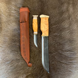 Dubbelkniv med huggare och kniv i masurbjörk (ej egen tillverkning) Den har nitad horntopp och mässingavslut på skaftet mot knivbladet. Huggarens längd i fodral är 37 cm varav knivbladet är 21 cm. Bladets bred är 38 mm. Knivens längd är 19,5 cm varav bladet är 7,7 cm. Brun läderslida med en ren som dekoration. Med knivarna på plats i slidan ger 37 cm längd. Huggaren är ett bra redskap istället för yxan och lätt att bära på bältet under tur i skog och mark. 