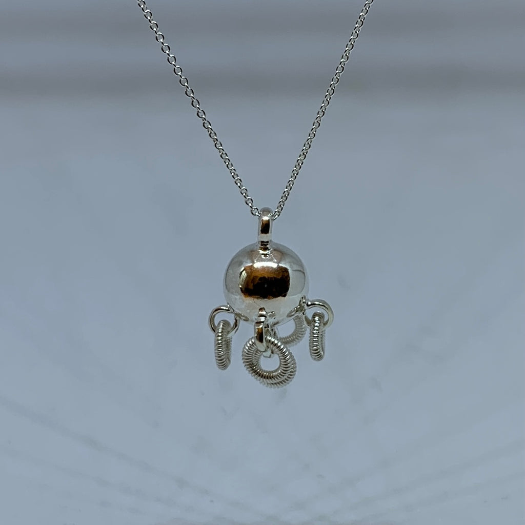 Komsekula i silver med fem små ringar. Diameter 10 mm. Silverkedja i silver 45 cm. Komsekulan är ett samiskt kultursmycke. Finns hos Risjfells Sameslöjd, Vilhelmina i södra Lappland