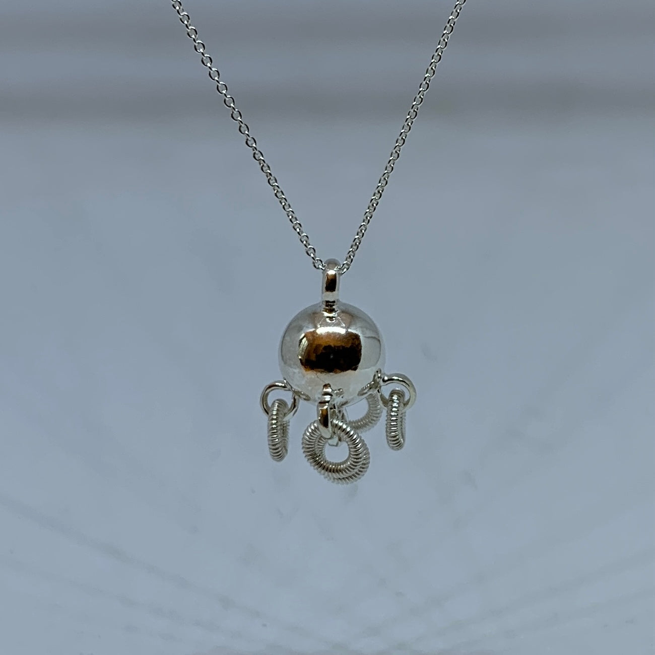 Komsekula i silver med fem små ringar. Diameter 10 mm. Silverkedja i silver 45 cm. Komsekulan är ett samiskt kultursmycke. Finns hos Risjfells Sameslöjd, Vilhelmina i södra Lappland