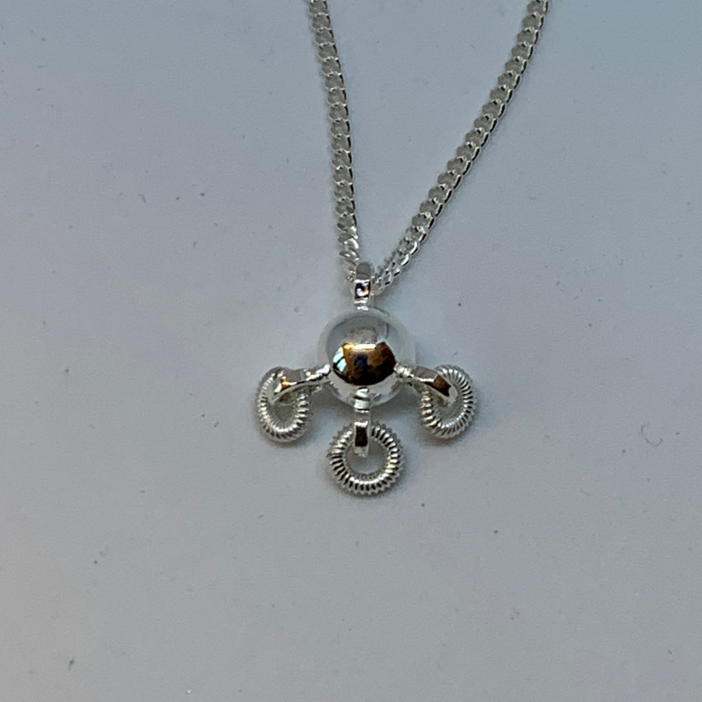 Söt komsekula i silver med tre små lindade ringar hängande på undersidan av kulan. Silverkedjan är 42 cm lång. Kulans diameter är 7 mm. Komsekulan är ett samiskt kultursmycke. Finns hos Risfjells Sameslöjd i Vilhelmina, södra Lappland.