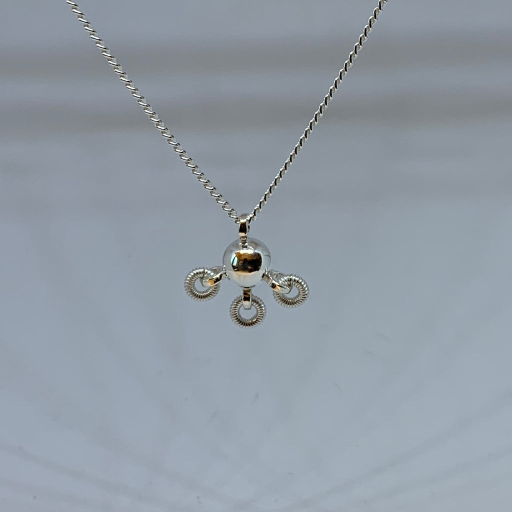 Söt komsekula i silver med tre små lindade ringar hängande på undersidan av kulan. Silverkedjan är 42 cm lång. Kulans diameter är 7 mm. Komsekulan är ett samiskt kultursmycke. Finns hos Risfjells Sameslöjd i Vilhelmina, södra Lappland.