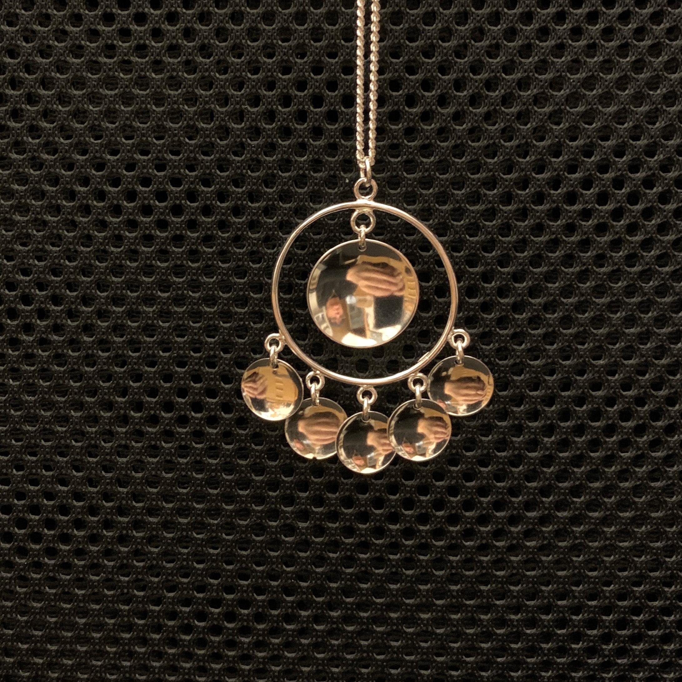 Halsband Solglitter i silver. Smycket är i samisk design. Diameter 32 mm. Längd 50 mm.  I nedre delen av ringen sitter fem konkava runda hängen och i mitten av ringen sitter ett stort konkavt runt hänge. Medföljande silverkedja mäter 60 cm. Finns hos Risfjells Sameslöjd i Vilhelmina, södra Lappland.