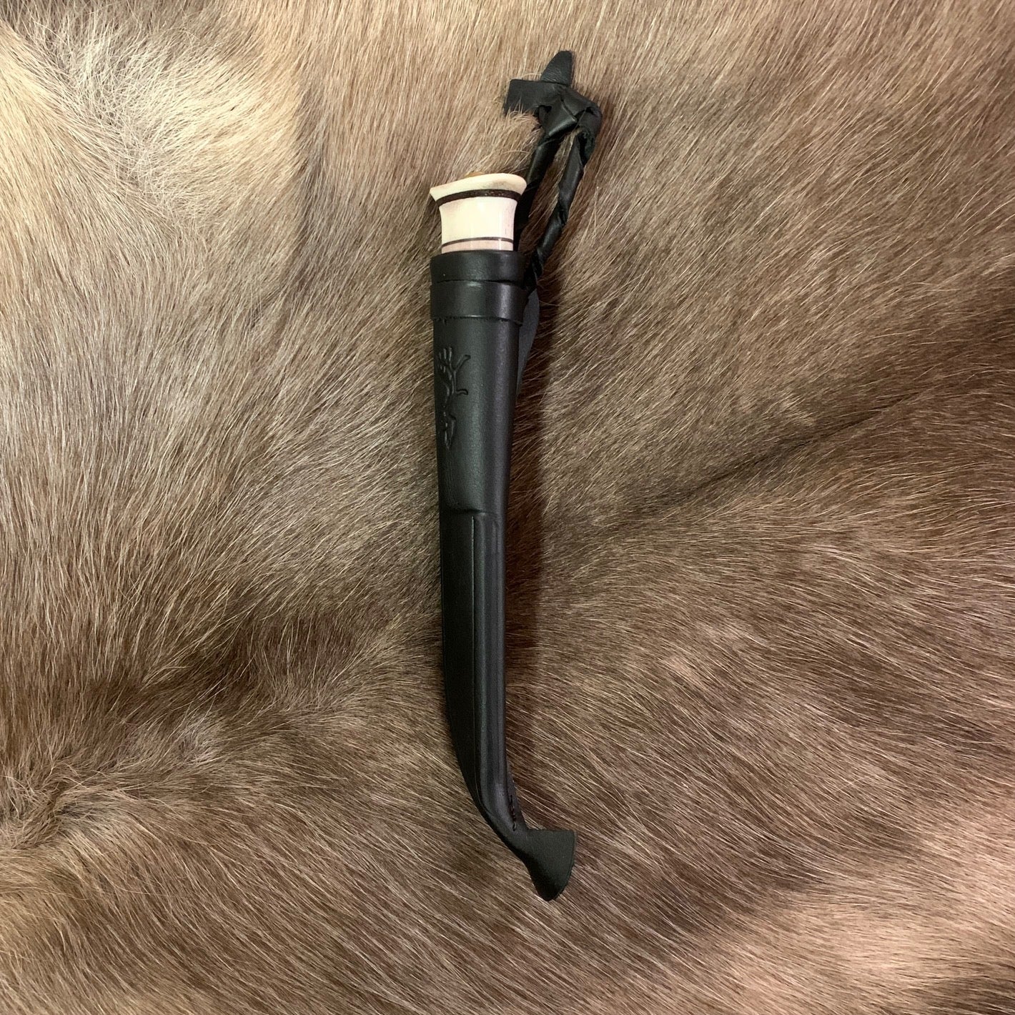 Jakt och fiskekniv (ej egen tillverkning)med hamrat blad 95 mm i kolstål. Knivskaftet gjord i masurbjörk och renhorn, nitad i topp. Mässing i nit och närmast knivbladet i skaftet. Skaftet har två fält horn med sex mörka inlägg.Svart läder i knivslidan som har en ren tryckt som dekoration. Knivens längd 21 cm och med hölster 25 cm. Finns hos Risjfells Sameslöjd i Vilhelmina