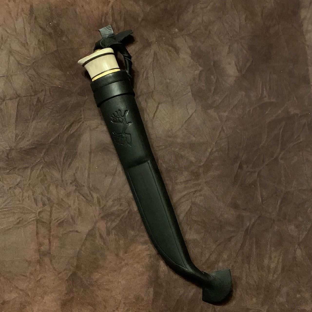  Jakt och fiskekniv (ej egen tillverkning)med slätt blad 95 mm i kolstål. Knivskaftet gjord i masurbjörk och renhorn i två fält. Nitad i topp. Mässing i nit och närmast knivbladet i skaftet. Svart läder i knivslidan som har en ren tryckt som dekoration. Knivens längd 21 cm och med hölster 25 cm. Finns hos Risfjells Sameslöjd i Vilhelmina.