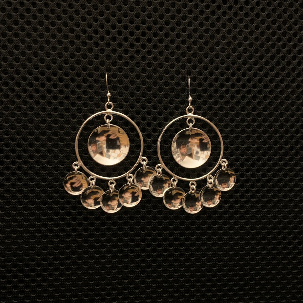 Örhängen Solglitter samisk design i silver stor modell. Diameter 32 mm. Längd 50 mm plus krok. Fem små konkava hängen i nedre kant och ett stort konkavt hänge i mitten. Finns hos Risfjells Sameslöjd, Vilhelmina