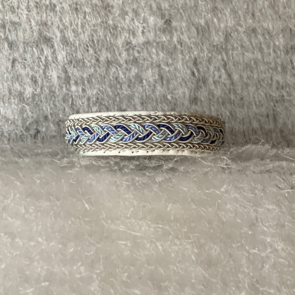 Tenntrådsarmband Vårjokk med flätning av tenntråd och blått, vitt och turkos tvinnat  på vitt renskinn. Knapp i renhorn och ögla i tvinnat renskinn. Bredd ca 10 mm. Samiskt hantverk av Doris Risfjell, Risjfells Sameslöjd i Vilhelmina.