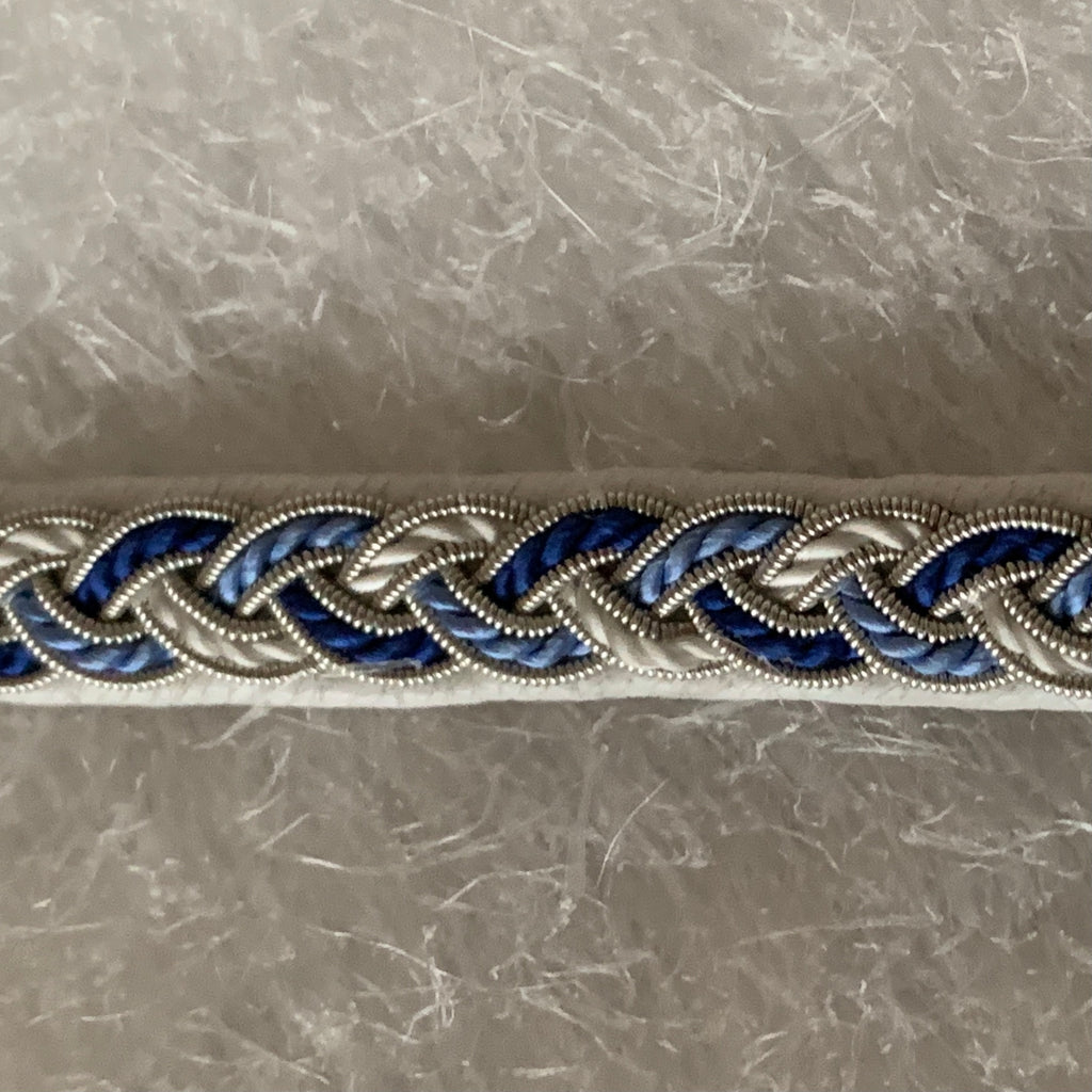 Tenntrådsarmband Vinterjokk med flätning av tenntråd och tvinnat blått och vitt garn på vitt renskinn. Knapp i renhorn och ögla i tvinnat renskinn. Bredd ca 10 mm. Samiskt hantverk av Doris Risfjell, Risfjells Sameslöjd Vilhelmina.