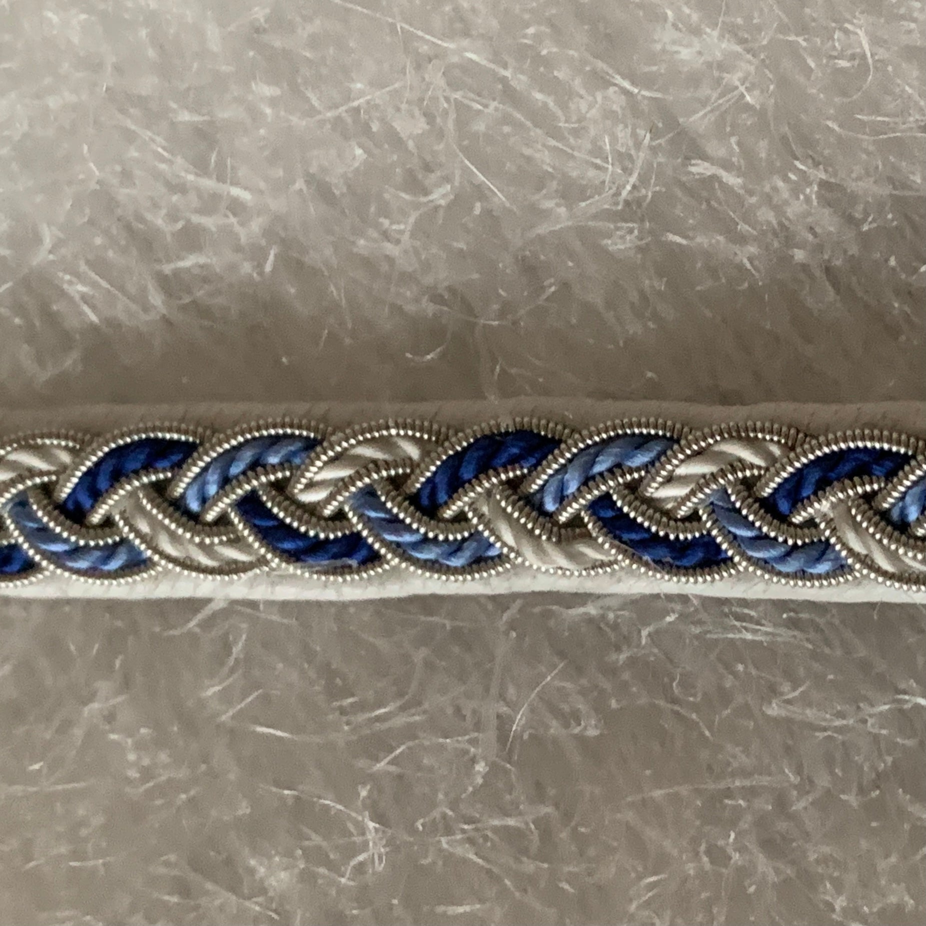 Tenntrådsarmband Vinterjokk med flätning av tenntråd och tvinnat blått och vitt garn på vitt renskinn. Knapp i renhorn och ögla i tvinnat renskinn. Bredd ca 10 mm. Samiskt hantverk av Doris Risfjell, Risfjells Sameslöjd Vilhelmina.